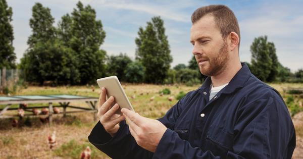 A farmer outside in blue overalls looking at his tablet
