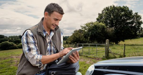A young farmer making notes on his tablet by his vehicle