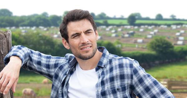 A young farmer in a checkered shirt leaning on a fence